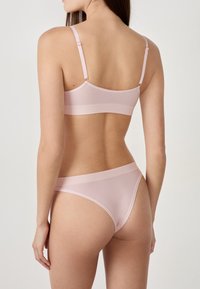 Helles rosa Bralette- und String-Set aus glattem Stoff. Das Bralette verfügt über verstellbare Träger und ein einfaches, nahtloses Design.