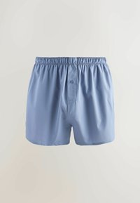 Világoskék férfi boxeralsó, gumis derékrésszel és egygombos sliccel, egyszínű világos háttér előtt bemutatva.