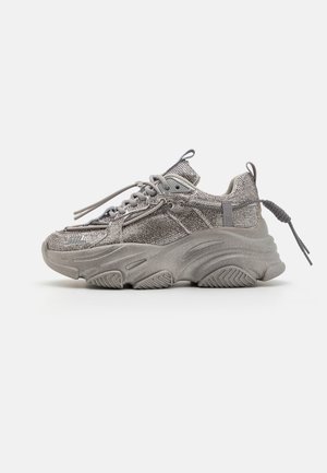Stevige grijze sneaker met een gestructureerde mesh bovenkant, dikke rubberen zool en platte veters. Heeft een gewatteerde kraag en hiel lus voor een veilige pasvorm.