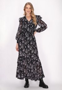 Schwarzes langärmliges Blumenkleid mit einem gestuften Design, rüschend Akzenten und einer taillierten Taille, kombiniert mit klobigen schwarzen Stiefeln.