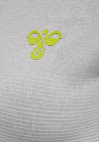 Żółte stylizowane logo pszczoły z geometrycznymi kształtami na jasnoszarym teksturowanym tle tkaniny.