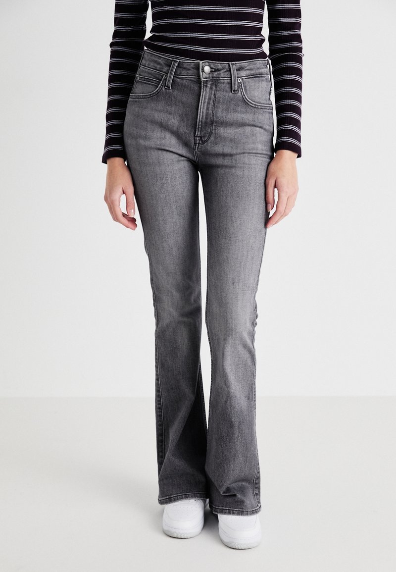 Jeans grises de campana con cintura alta, que presentan un diseño clásico de cinco bolsillos y sutiles variaciones de lavado, combinados con zapatillas blancas.