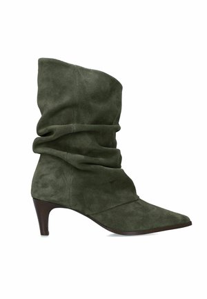 Donkergroene suède midkuit laars met losse pasvorm, puntige neus en smalle bruine hoge hak.