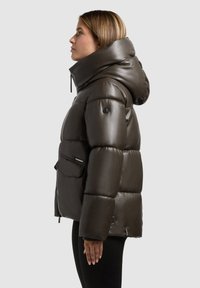 Bunda do deště v tmavě hnědé barvě, s vysokým límcem, lesklým povrchem, kapsou na zip a silně prošívanými sekcemi pro izolaci.