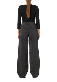 Schwarzes Rippenshirt kombiniert mit lockeren, hochgeschnittenen, dunkelgrauen Jeans. Die Jeans verfügen über Gesäßtaschen und haben einen entspannten, weit geschnittenen Stil.