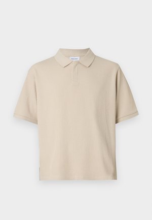 Béžové polo tričko s krátkym rukávom z rebrovanej látky. Má klasický golier a zapínanie na tri gombíky, s mierne oversize strihom.