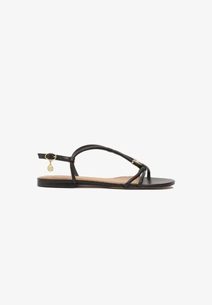 Las sandalias planas negras cuentan con un diseño de tiras delgadas, una correa de tobillo ajustable con herrajes dorados y una textura de cuero suave.