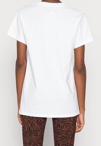 Vit bomullströja med korta ärmar och rak skärning. Enfärgad tyg utan mönster, sedd från baksidan. Bruna leggings med tigerrand.