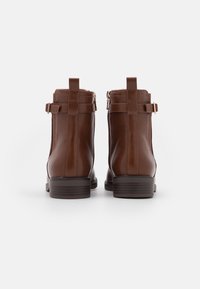 Brown leather ankle boots with side zippers, rounded toes, and chunky heels. Features horizontal stitching and decorative straps.