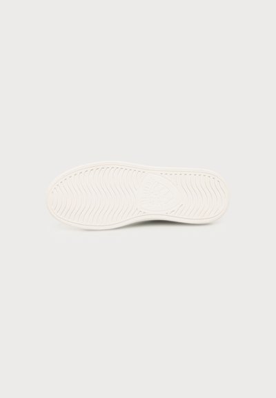 White sneaker sole with wavy tread pattern and shield-shaped logo in the center on a plain light background.