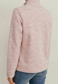 Roze textuur fleece jack met een hoge kraag en lange mouwen, met een subtiel gemarmerd patroon en een rechte zoom. Gedragen met blauwe jeans.