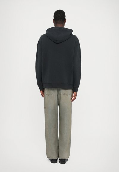 Črna kapuca s sproščenim krojem, v kombinaciji z svetlo sivo širokima hlačami z rahlo teksturo in zadnjimi žepi.