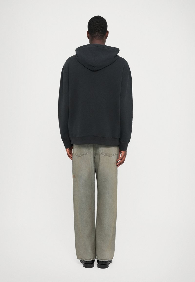 Schwarzer Hoodie mit lockerer Passform, kombiniert mit hellgrauen weit geschnittenen Jeans, die eine dezente Textur und Gesäßtaschen haben.
