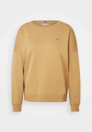 Senfgelber Pullover mit Rundhalsausschnitt, überschnittenen Schultern und gerippten Bündchen. Mit kleinem Logo auf der linken Brust. Weiche Stoffstruktur.