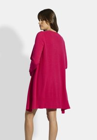 Cárdigan largo de punto en un vibrante color rosa, con apertura frontal. Presenta puños y dobladillo acanalados, un corte relajado y un diseño ligeramente acampanado.