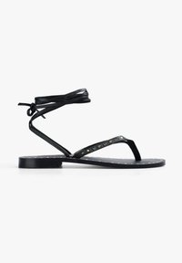 Sandal in pelle nera con un design minimalista. Presenta cinturini sottili, lacci alla caviglia e una suola piatta con piccoli chiodini dorati su un motivo a pois.