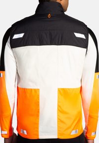 Gilet de sécurité avec une partie supérieure noire, un milieu blanc et une partie inférieure orange vif. Des accents réfléchissants sur les manches améliorent la visibilité.