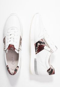 Sneaker bianco in pelle con un accento in stampa rettile rossa e nera testurizzata, cerniera laterale e suola in gomma chiara.