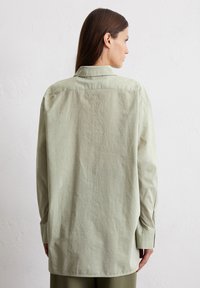 Light green, oversized long-sleeve shirt with a classic collar and buttoned cuffs; soft, textured fabric with a slightly wrinkled appearance.