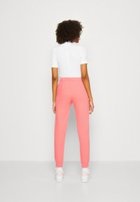 Rosa joggers med elastisk midja och muddar, ihop med en vit t-shirt med kort ärm. Tyget verkar mjukt och avslappnat, perfekt för hemmabruk.