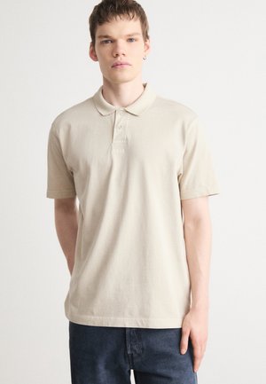 Beige Polohemd aus Baumwolle, mit Kragen, drei Knöpfen und kleinem Logo auf der Brust. Kurze Ärmel und entspannte Passform.