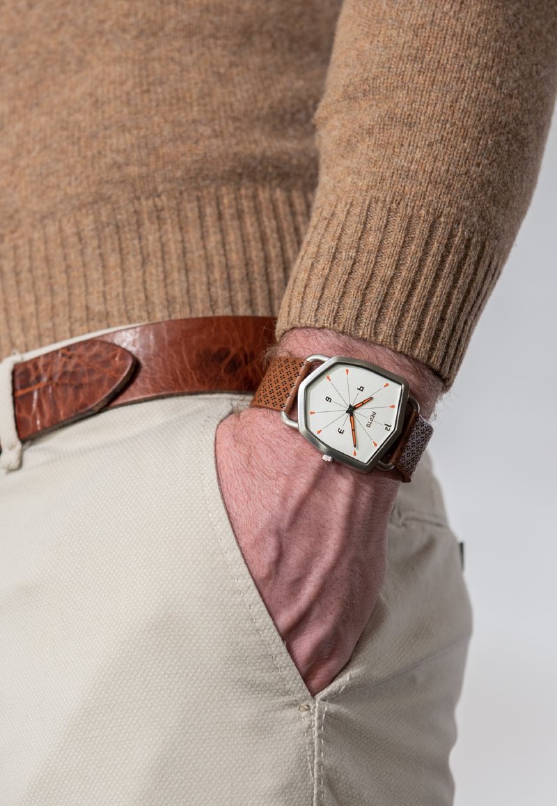 Brun læderrem ur med et hexagonalt sølvgehus, hvid urskive, orange detaljer og brun tekstureret udsmykning, båret på et håndled.