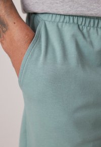 Pantalones cortos de algodón en azul claro con ceñidor elástico, que presentan un bolsillo lateral visible a lo largo de la costura y una textura suave.