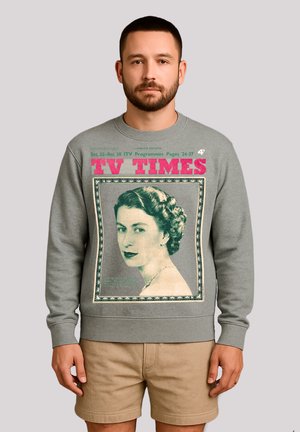 Mann mit kurzem Bart, der ein graues Sweatshirt trägt, das ein Vintage- TV Times-Cover mit einem Porträt einer Frau und rot gefärbtem Text zeigt.