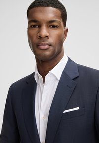 Marineblauer Anzug mit Muster und Kerbkragen, kombiniert mit einem weißen Hemd mit spitzem Kragen und einem Einstecktuch.