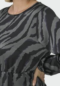 Mekko, joka on musta ja harmaa, zebra-raitasuunnittelu, jossa on pyöreä kaula-aukko ja puffihihat. Valmistettu sileästä, pehmeästä kankaasta.