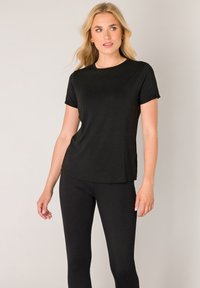 Schwarzes T-Shirt mit kurzen Ärmeln aus weichem Stoff, mit rundem Ausschnitt und lockerem Schnitt. Trägt dazu schwarze Leggings, die eine glatte Textur zeigen.