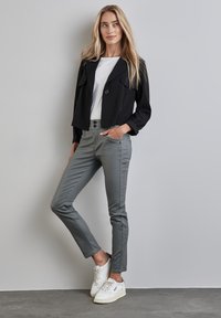 Svart kort jacka med ficklock, vit t-shirt, grå kroppsnära byxor och vita sneakers på en grå bakgrund. Släta texturer, avslappnad stil.