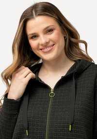 Felpa nera con zip e motivo a griglia testurizzato, hardware della zip verde e lacci abbinati. Tessuto morbido con vestibilità comoda.