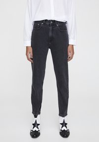 Black denim jeans with a high waist and tapered leg. Paired with a white button-up shirt and star-patterned black and white boots.