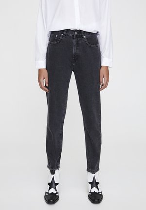 Zwarte denim jeans met een hoge taille en een taps toelopende pijp. Gecombineerd met een witte button-up shirt en zwart-witte laarzen met sterpatroon.