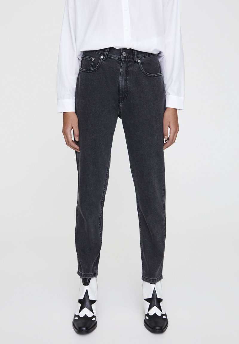 Black denim jeans with a high waist and tapered leg. Paired with a white button-up shirt and star-patterned black and white boots.