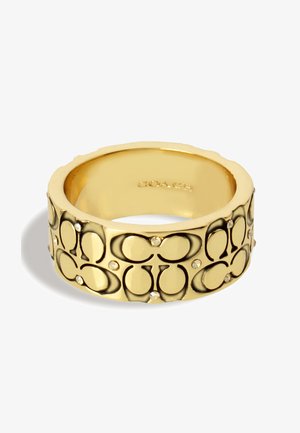 Kultaketju, jossa on kohokuvioitu kuosi ja pieniä kirkaita kristalleja. Sileä sisäosa, teksturoitu ulkopinta, jossa on päällekkäin olevia logoja. Kiiltävä pinta.