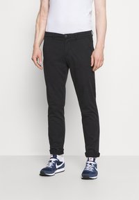 Zwarte katoenen broeken met een slim fit, opgerolde manchetten en een enkele knoopsluiting, gecombineerd met marineblauwe sneakers en witte sokken.