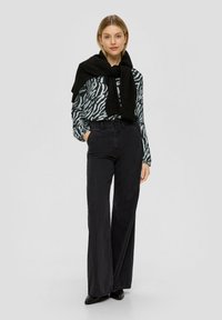 Langarmshirt mit einem schwarz-weißen Zebra-Muster, kombiniert mit hochgeschnittenen schwarzen Schlagjeans und einem schwarzen Strickschal.