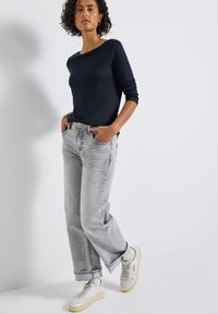 Marineblauwe blouse met lange mouwen gecombineerd met lichtgrijze, loose-fit jeans en witte sneakers. De outfit heeft minimale patronen en eenvoudige ontwerpelementen.