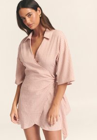 Roze geruite wikkeljurk met korte mouwen, een kraag en een zijstrikdetail. Heeft een gestructureerde stof en een golvende zoom.