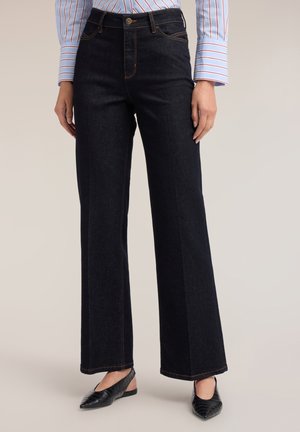 Mujer con vaqueros negros de tiro alto y pierna ancha combinados con zapatos slingback negros de punta afilada y una camisa de botones con rayas.