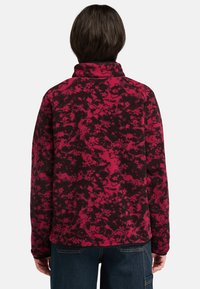 Pullover in pile con motivo astratto rosso e nero. Presenta un colletto alto e maniche lunghe con una vestibilità comoda, realizzato in tessuto testurizzato.