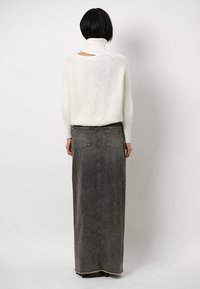 Witte gebreide trui met hoge kraag en open rugdetail, gecombineerd met een lange grijze jeansrok met achterzakken en een rafelige zoom.