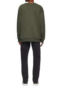 Olivgrüner Sweatshirt, lockere Passform, gerippte Bündchen und Saum, weiche Textur. Kombiniert mit schwarzen Jeans und weißen Sneakers. Vorderansicht nicht sichtbar.