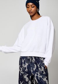 Felpa bianca a maniche lunghe e taglio corto con un logo discreto. Abbinata a pantaloni della tuta blu navy con un motivo e una texture particolare.