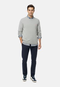 Suéter gris sobre una camisa de cuadros azul, pantalones azul marino y zapatillas azul marino. El suéter cuenta con un pequeño logo rosa. Tejido suave, corte relajado.