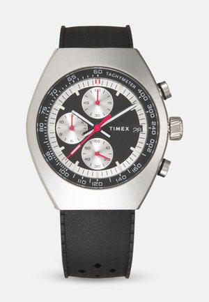 Srebrny zegarek ze stali nierdzewnej z czarną tarczą, czerwonymi akcentami, skalą tachymetryczną i teksturowanym czarnym paskiem gumowym. Posiada trzy sub-tarczki.