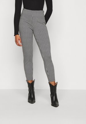 Schwarz-weiße Hahnentrittmuster-Hosen mit hoher Taille und schmaler Passform, kombiniert mit schwarzen Knöchelstiefeln. Glatte Stofftextur.