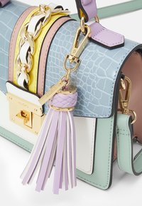 Sac à main en couleurs pastel avec une texture croco bleu clair, chaîne dorée, pompon lavande et fermoir doré de la marque "ALDO."